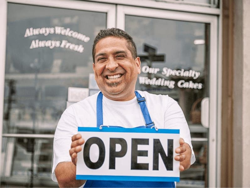 A latino small business owner holding an open sign.