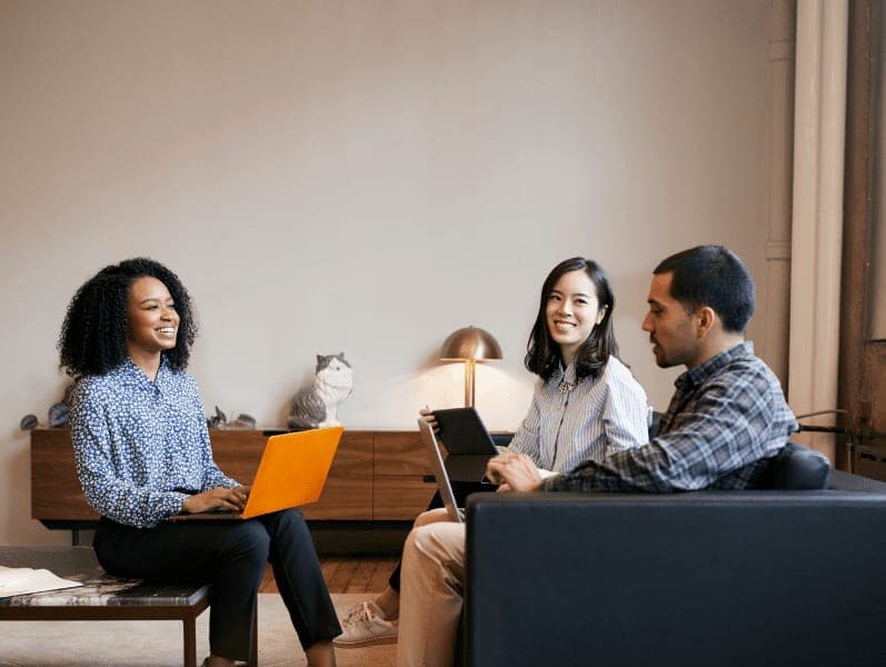 Smiling work colleagues using laptops at a casual meeting.