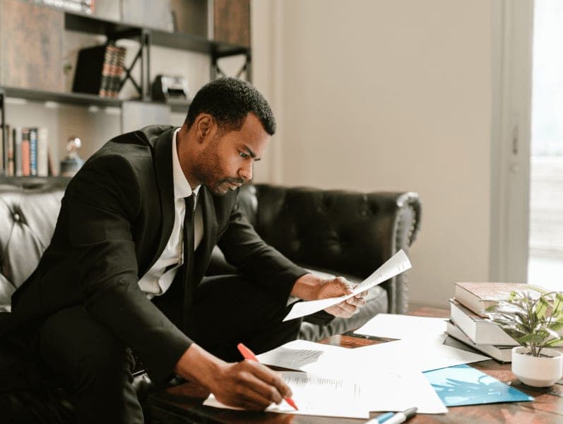 Man on black suit writing on paper.
