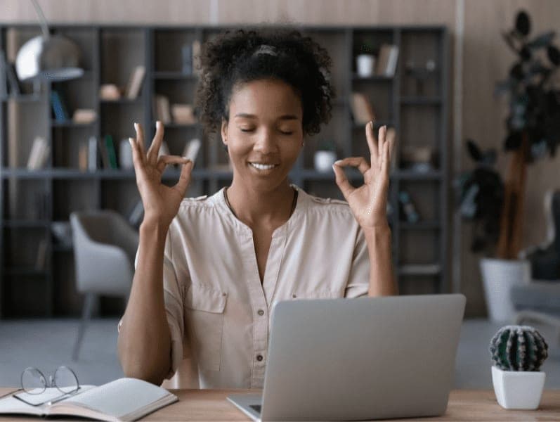 Smiling African-American woman meditating, sitting at work desk.