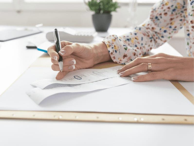 Accountant checking and comparing receipts while making a final report, working at her desk with calculator alongside.