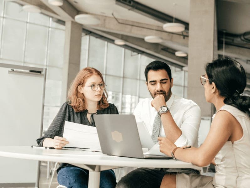 Three employees discussing project on laptop.