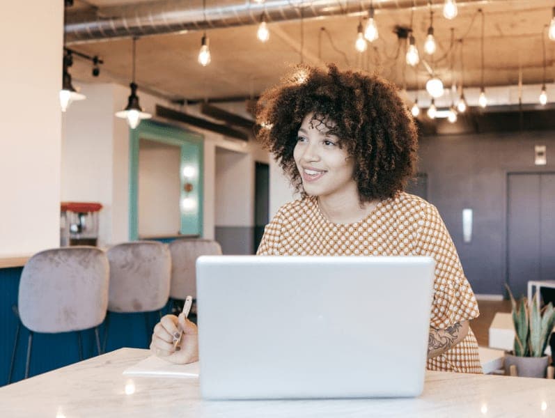 Woman looking far away, thinking of new ideas sitting at table with laptop.