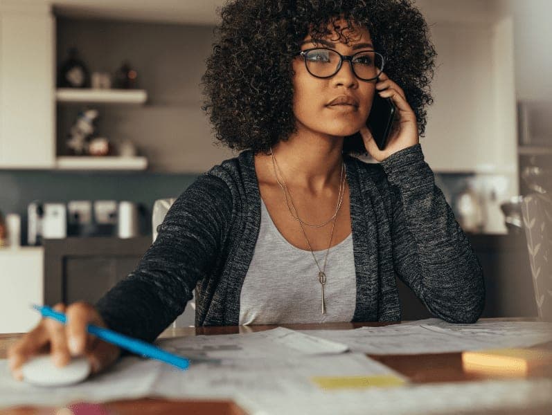 Woman using desktop computer and talking on cell phone.