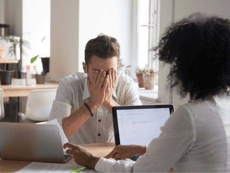 Businessman covering face with hands upset about bad news in document.