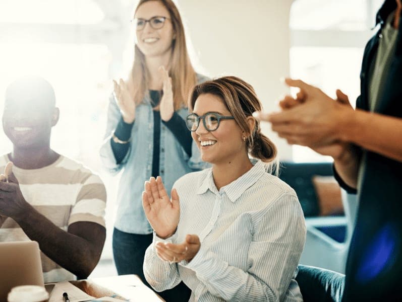 Group of diverse work colleagues clapping during a presentation while sitting together in a modern office