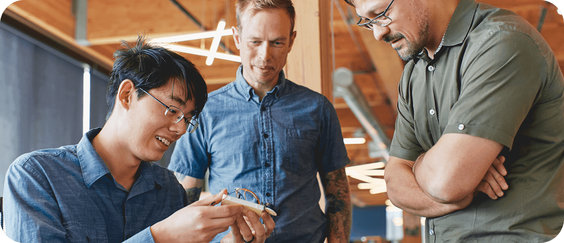 Three men examining a small electronic device together in a modern office setting, displaying teamwork and innovation.