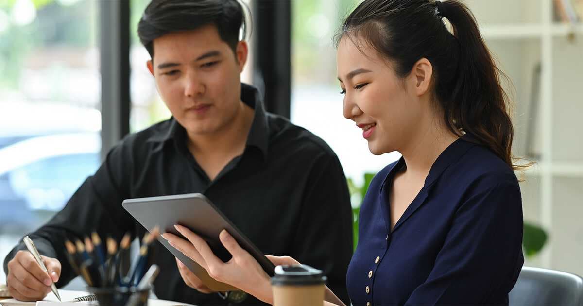 Two people sit in front of a tablet