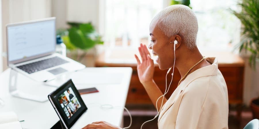 Side view of delighted black businesswoman with short blond hair smiling and waving hair while using tablet to call to colleagues from office