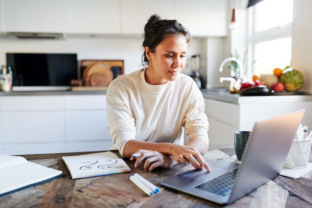 Creative young woman using a laptop to research some designs while sitting at her kitchen table at home