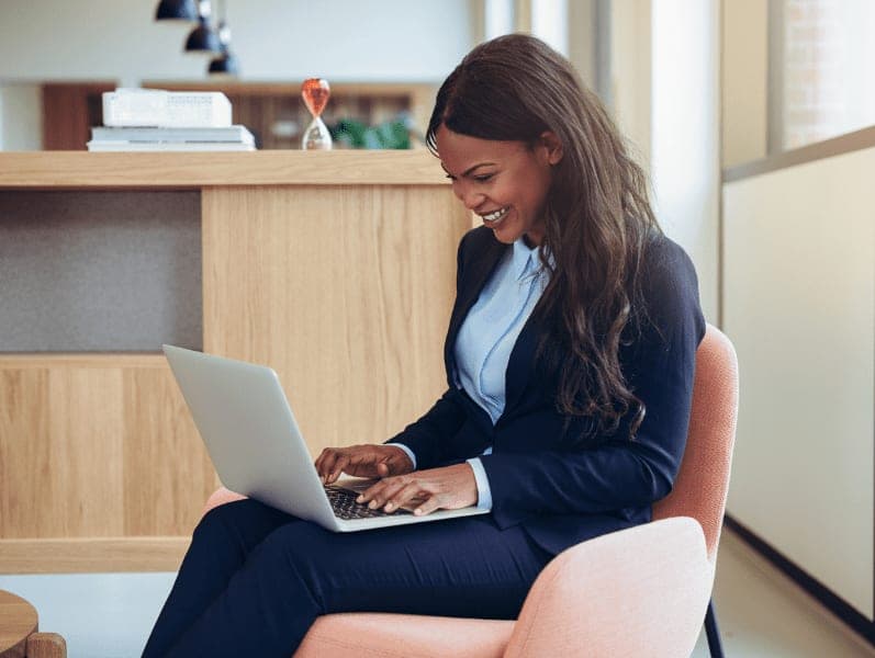 Young African-American businesswoman laughing while working online with a laptop in the lounge of an office.