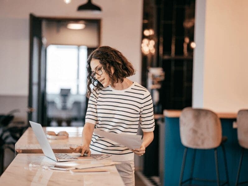 Woman standing at island table while working on her laptop and talking on her cell phone