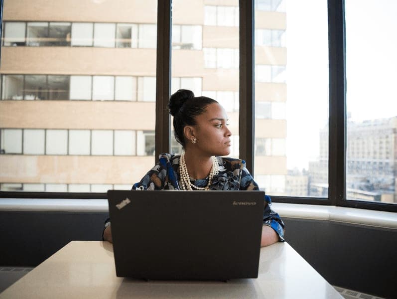 Woman looking out window as she sits feelin anxious in front of her laptop