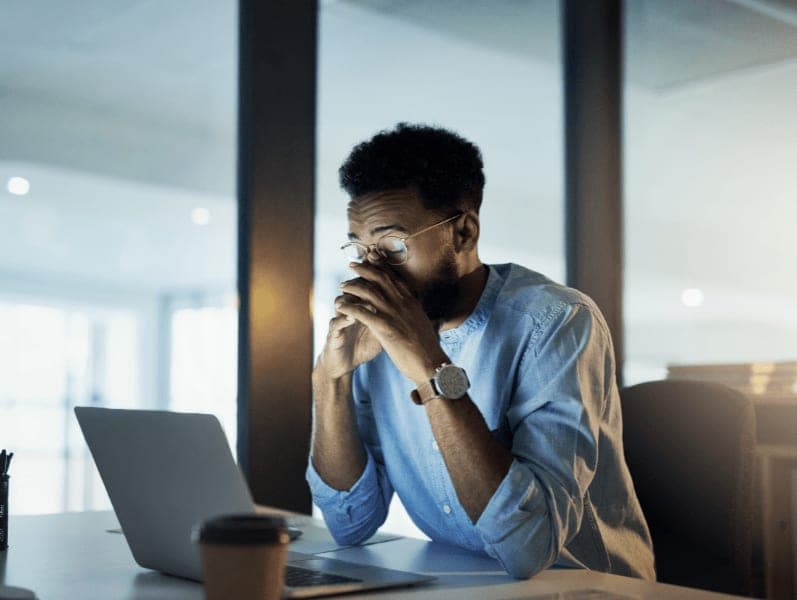 Man sitting in office area in front of lap top holding face in stress