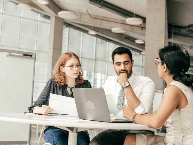 The team member sitting around table in front of lap top discussing