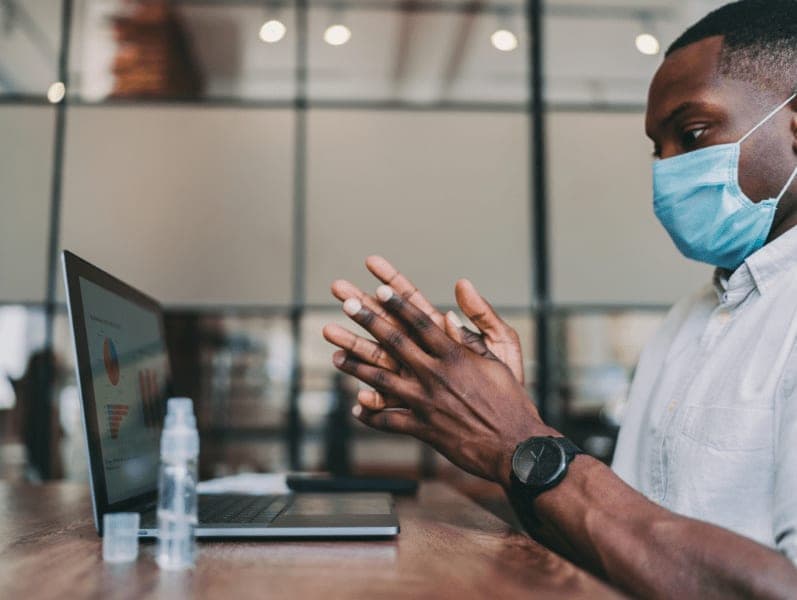 Man sitting at desk in front of the laptop with a mask on