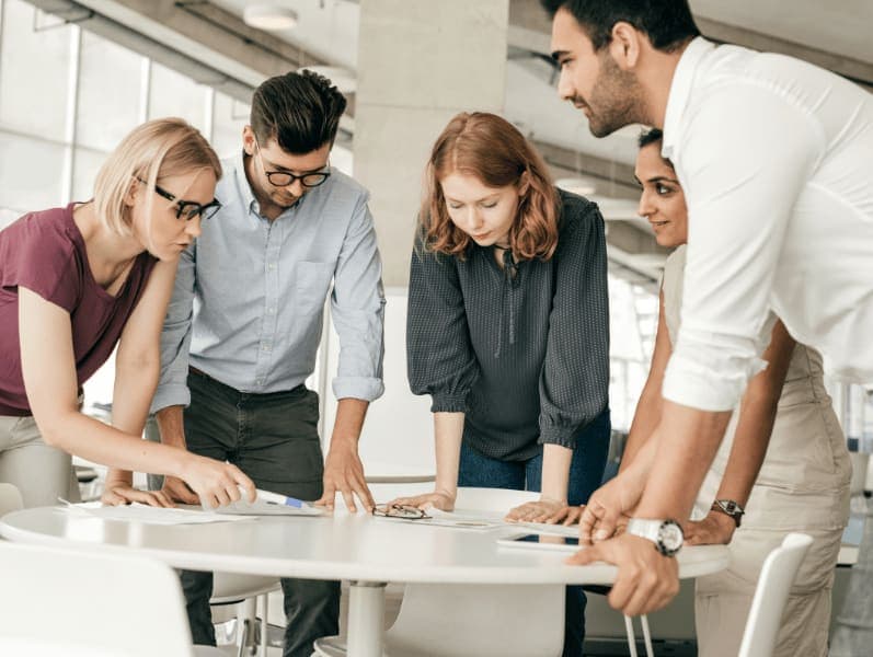 Group of male and females leaning over a table of content to review