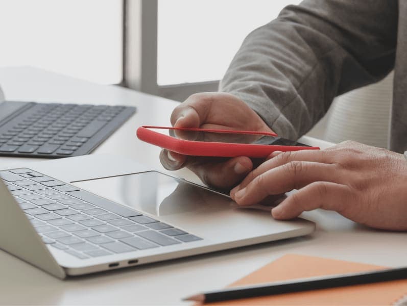 Man working on phone with two laptop in front of him with only has hands in view