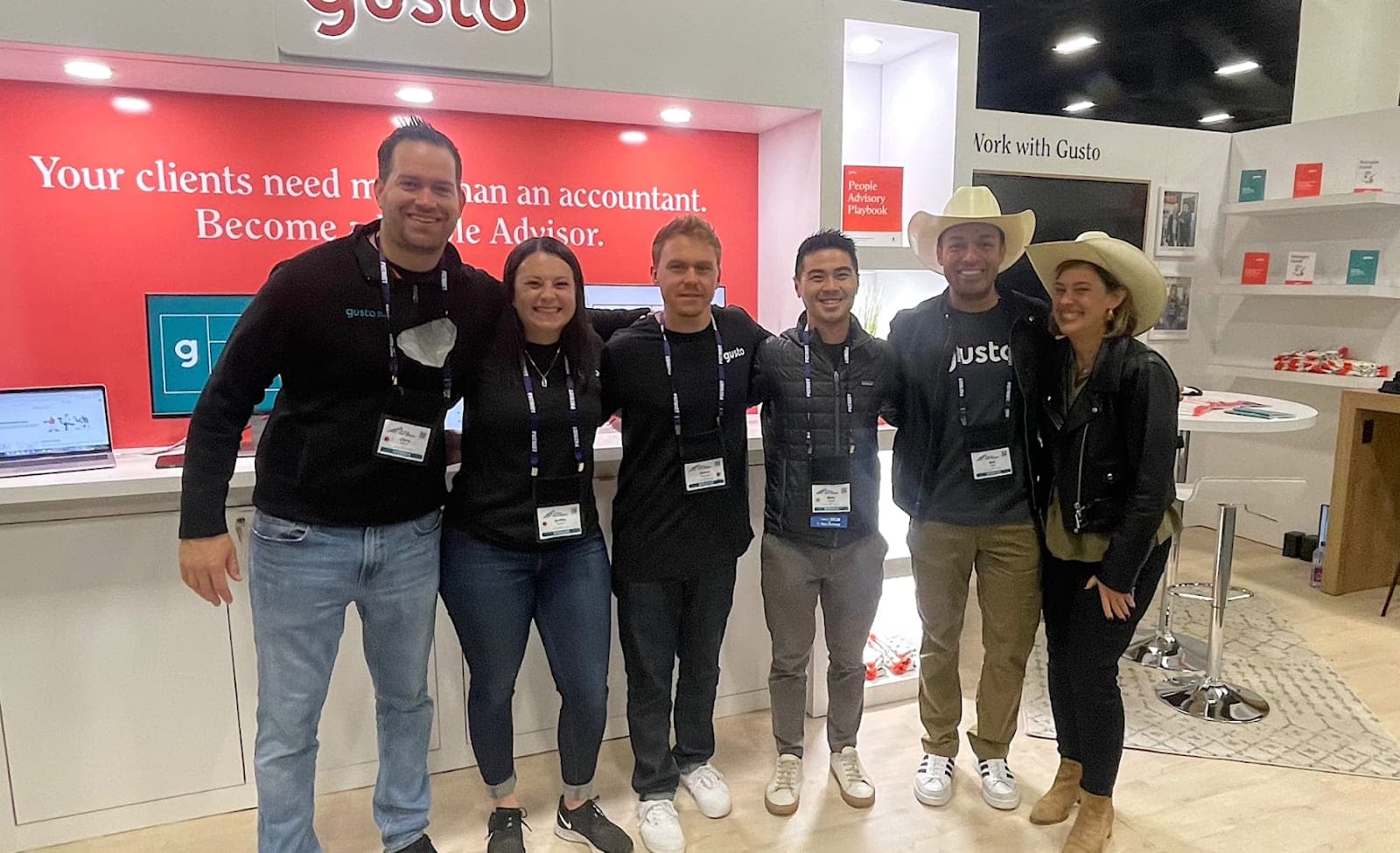 A group of Gusto coworkers stand in front of a Gusto booth