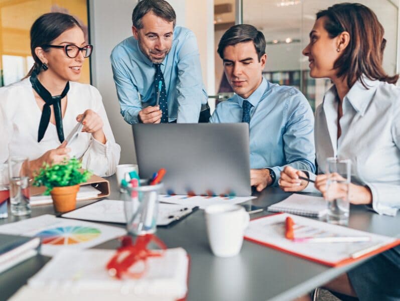 Team of employees half standing and half sitting around lap top discovering growth potential