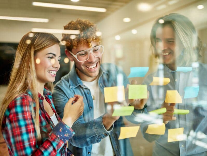 Young employees standing around glass white board reviewing sticky notes
