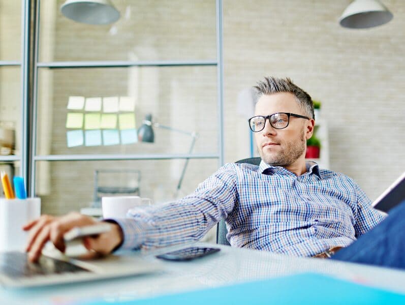 Man sitting back in desk chair referencing ipad