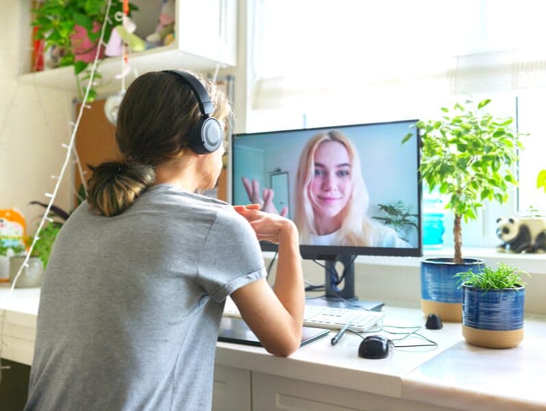 Young male sitting at desk from home facing desktop screen speaking to female colleague over video