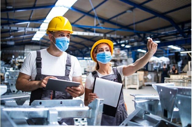 Male and Female wearing a safety hat and masks coordinating in a factory