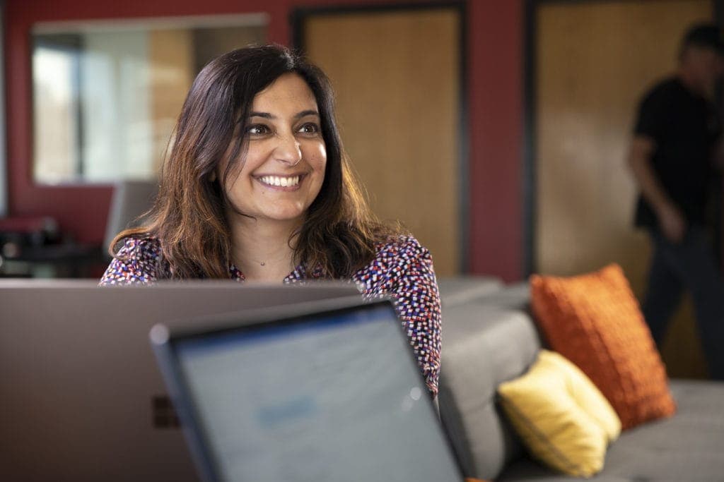 Woman sitting at a table with her computer smiling at another person