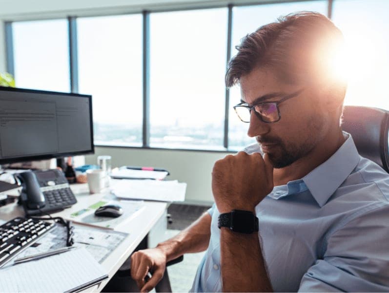 Businessman wearing spectacles sitting with hand to his chin.