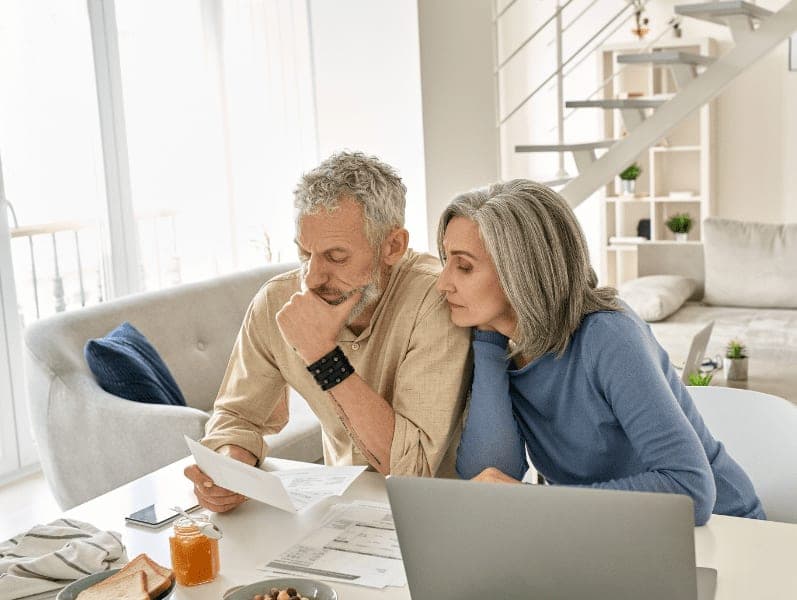 Worried senior couple checking bank documents at home.