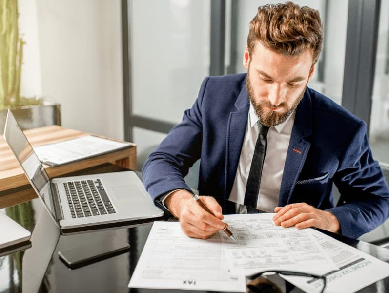 Tax manager dressed in the suit working with documents and laptop at the modern office.