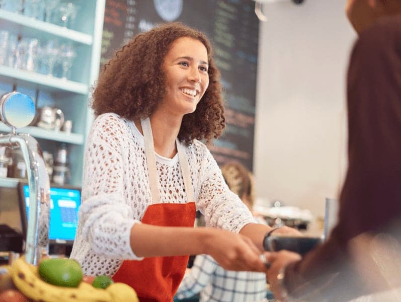 Barista hands over a coffee and cakes across the counter top of a cafe bar.