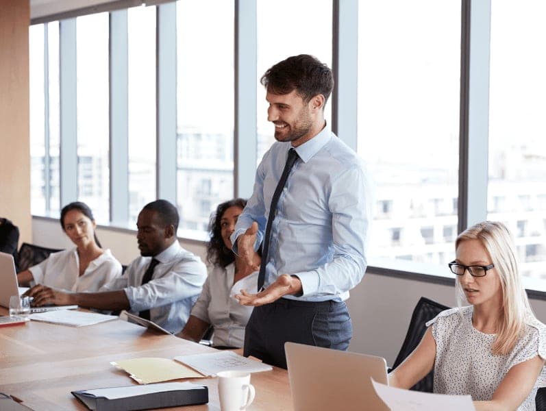 Businessman stands to address meeting around board table.