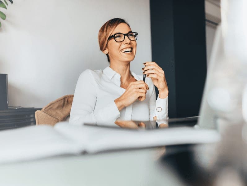 Woman sitting in office holding a pen in a happy mood.