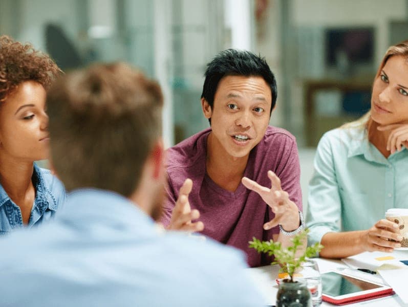 Group of business people talking together around a table in an office.