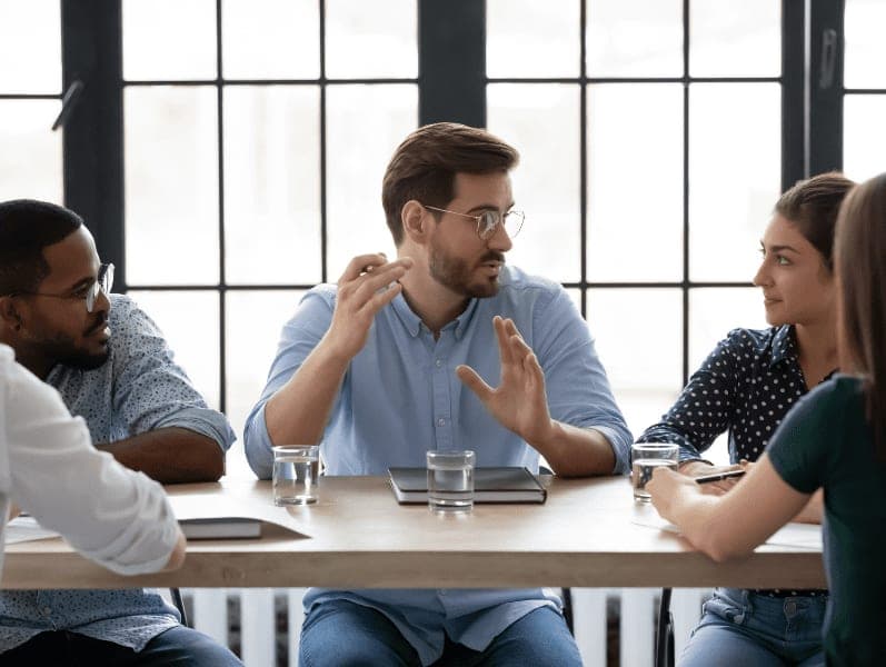 Employees listening to confident business coach at meeting.