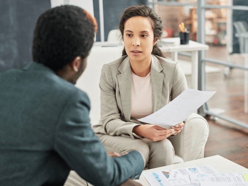 Serious young business lady with paper talking to customer during meeting in office.