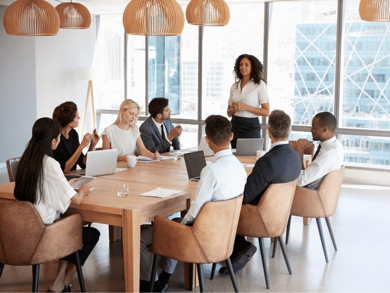 Businesswoman stands to address meeting around board table.