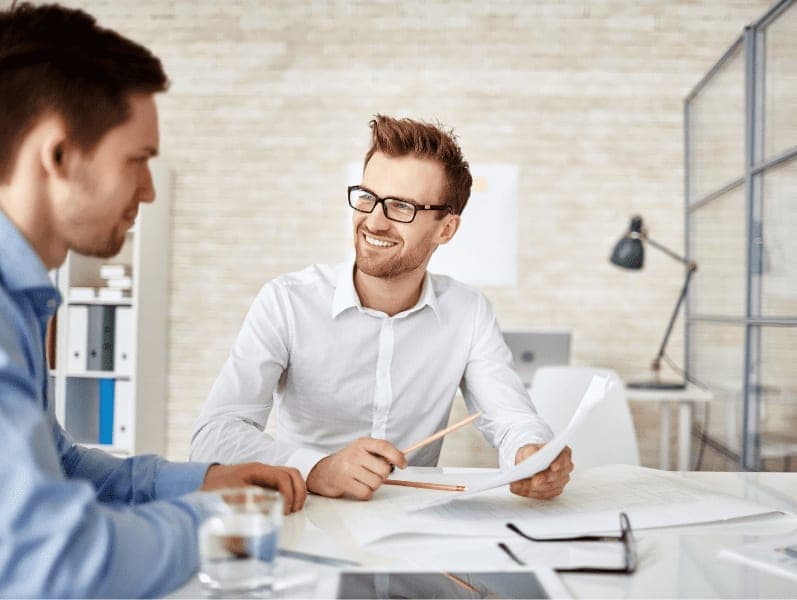 Young businessman looking at co-worker during explanation of document.