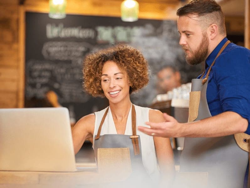 Two coffee shop owners having a discussion while looking at a laptop