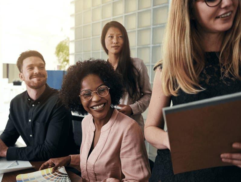 Group of diverse business colleagues smiling while working together around a desk in a modern office