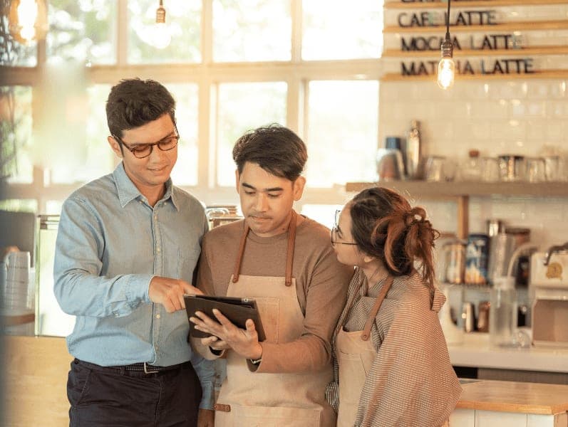 Couple business owners using a tablet having a discussion with a businessman in a coffee shop