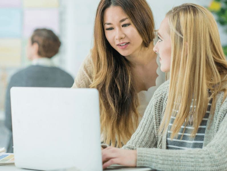 Two women discussing with each other while looking on laptop
