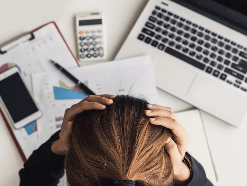 woman holding her head in front of messy desk