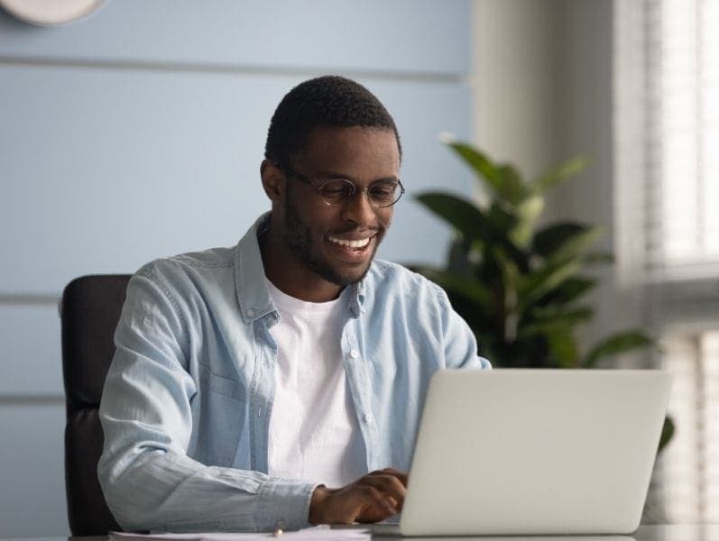 Middle aged male sitting at a desk in front of a lap top smiling