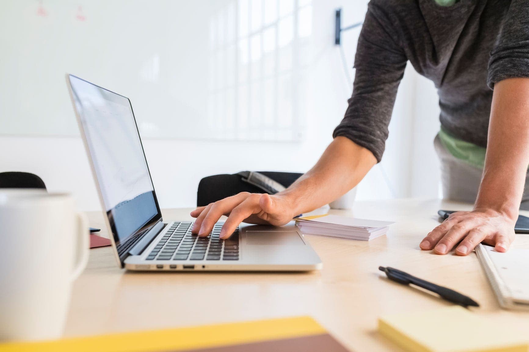 Man standing at a desk with a laptop backing up his data via the cloud.