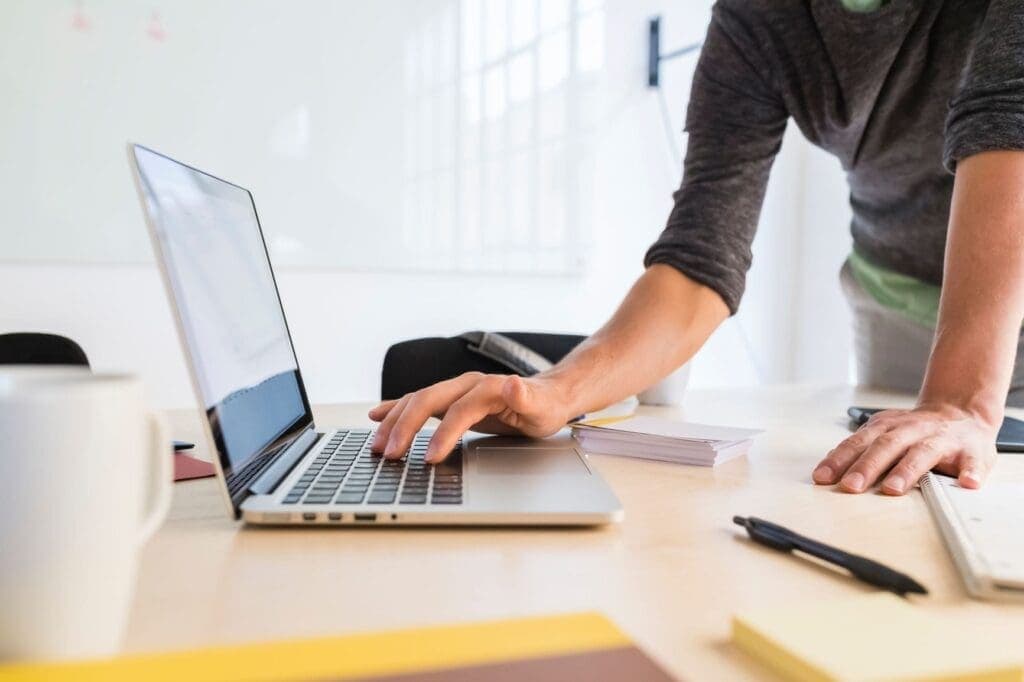 Man standing at a desk with a laptop backing up his data via the cloud.