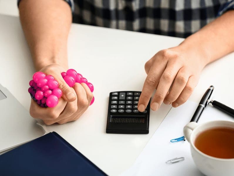 Man squeezing a stress ball and then using a calculator with the other