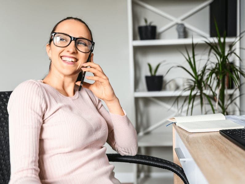 Woman sitting in home office chair speaking on her cell phone at desk
